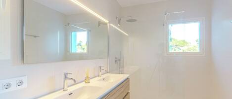 Une salle de bain moderne avec un grand miroir, deux lavabos, une douche et une fenêtre.