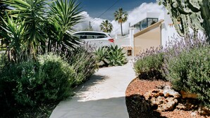 Un vialetto conduce a un edificio moderno con facciata bianca, immerso nel verde e con un'auto parcheggiata.