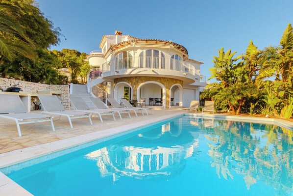Ein großes, luxuriöses Haus mit Swimmingpool, Sitzgelegenheiten im Freien und tropischer Bepflanzung.