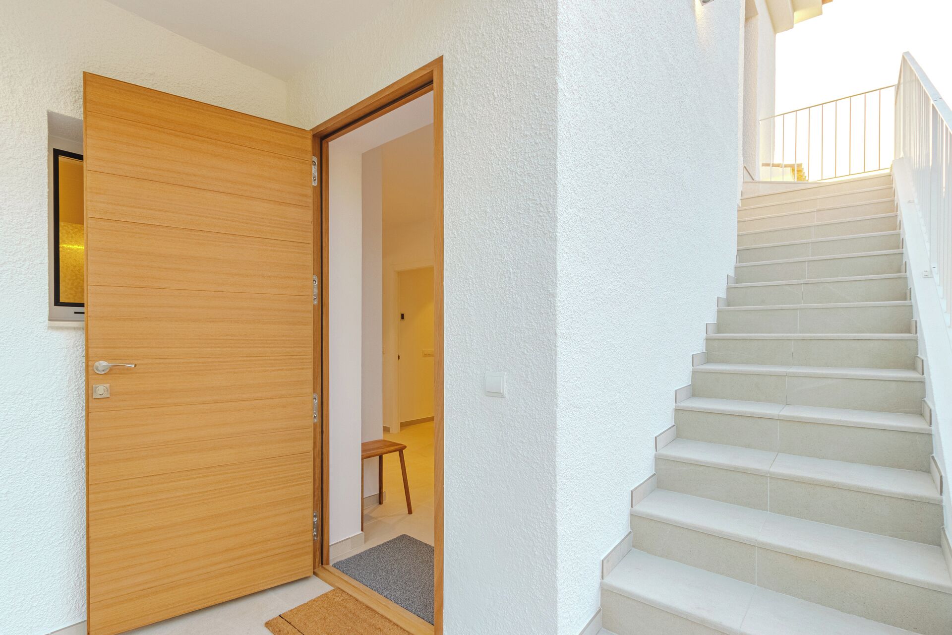A wooden door leading to a room with a small table and a chair, and a staircase with a railing.