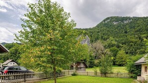 Paisagem rural com cerca de madeira, uma pequena construção rústica e um carro estacionado perto de uma casa.