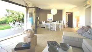 A spacious living area with a dining table and chairs, a sofa, and a large window offering a view of the outdoors. - VILLA DEL MARE IN CHIA, WITH POOL OVERLOOKING THE SEA AND TOWER (Domus de Maria loc. Chia)
