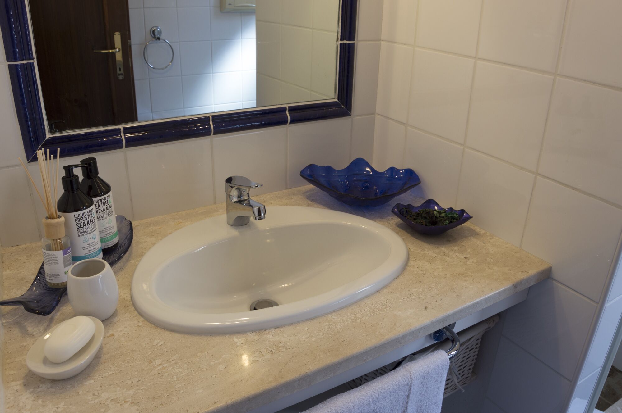 A bathroom with a white sink, a blue soap dish, a blue soap dispenser, a white cup, and a blue bowl on the countertop.