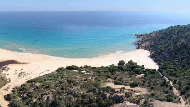 A coastal landscape with a beach, a tower on a hill, and dense vegetation. - VILLA DEL MARE IN CHIA, WITH POOL OVERLOOKING THE SEA AND TOWER (Domus de Maria loc. Chia)