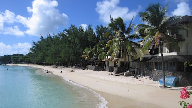 Een strand met helder turquoise water, een zandstrand en een rij gebouwen met balkons met uitzicht op het strand.