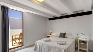 Ein Schlafzimmer mit einem großen Bett, zwei Nachttischen, einem Sessel und Blick ins Freie durch eine Schiebetür.