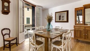 Ein Esszimmer mit einem Holztisch, gedeckt für vier Personen, umgeben von weißen Stühlen. Auf dem Tisch steht eine große Vase mit getrockneten Pflanzen.