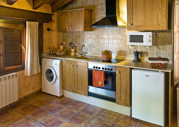 A compact kitchen with wooden cabinets, a washing machine, an oven, a microwave, and a small refrigerator.