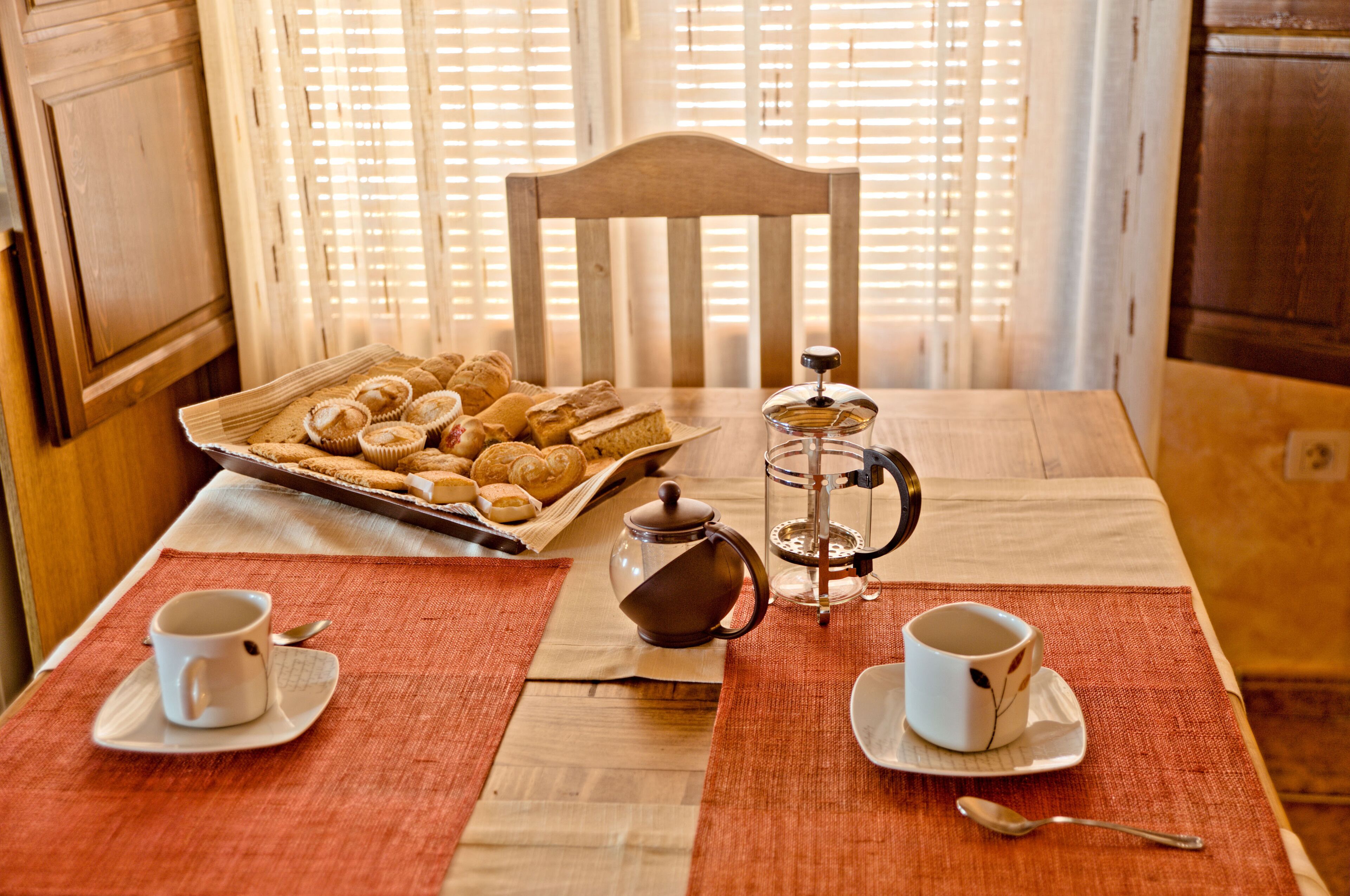 Une table dressée pour le petit-déjeuner, avec un plateau de viennoiseries, une cafetière et deux tasses.