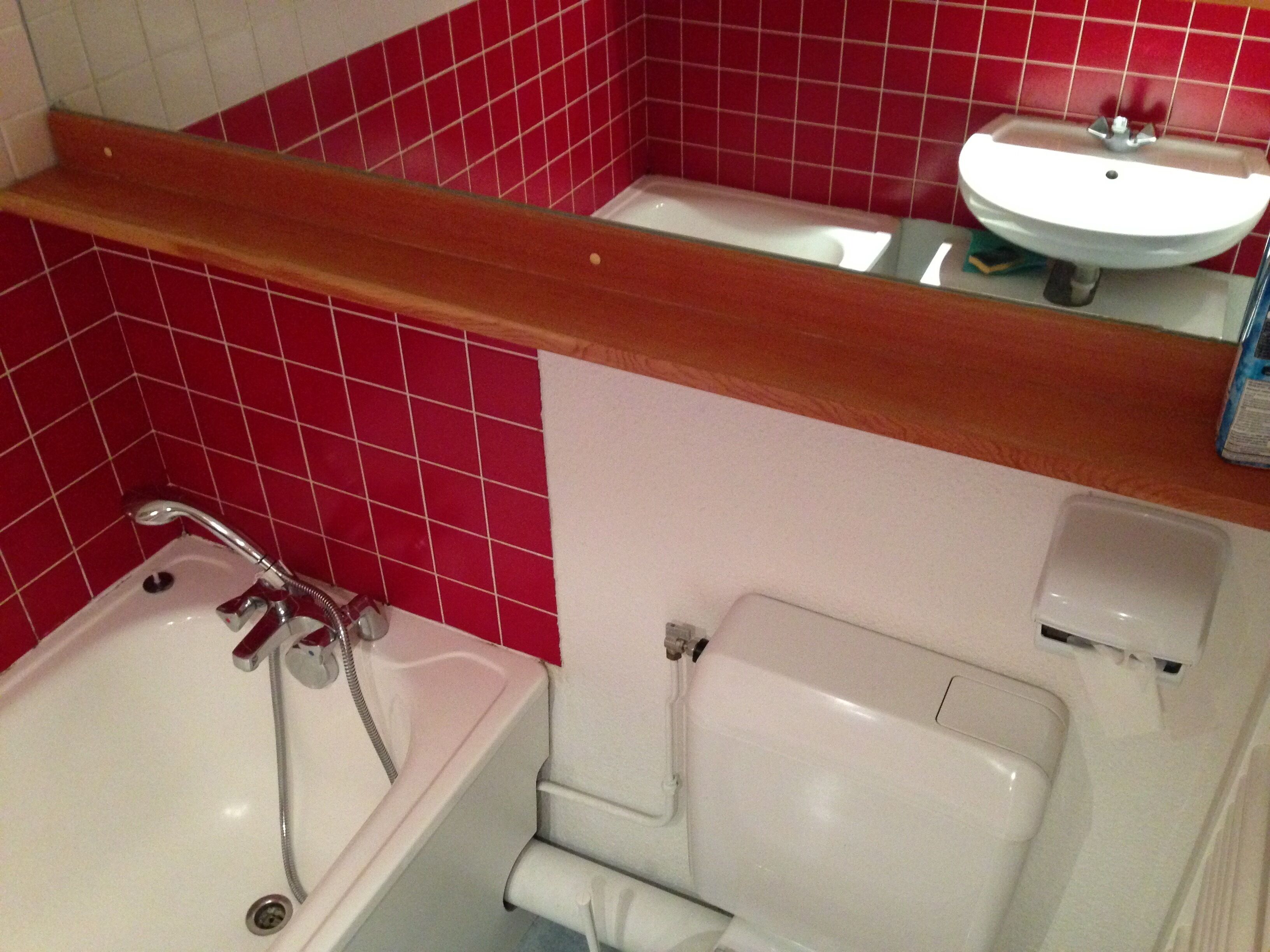Un baño con una bañera blanca, un inodoro blanco y un lavamanos blanco frente a una pared de azulejos rojos.
