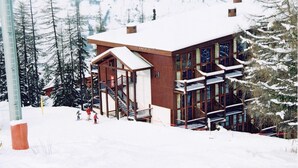 A wooden lodge with a staircase leading to a balcony, surrounded by snow-covered trees.