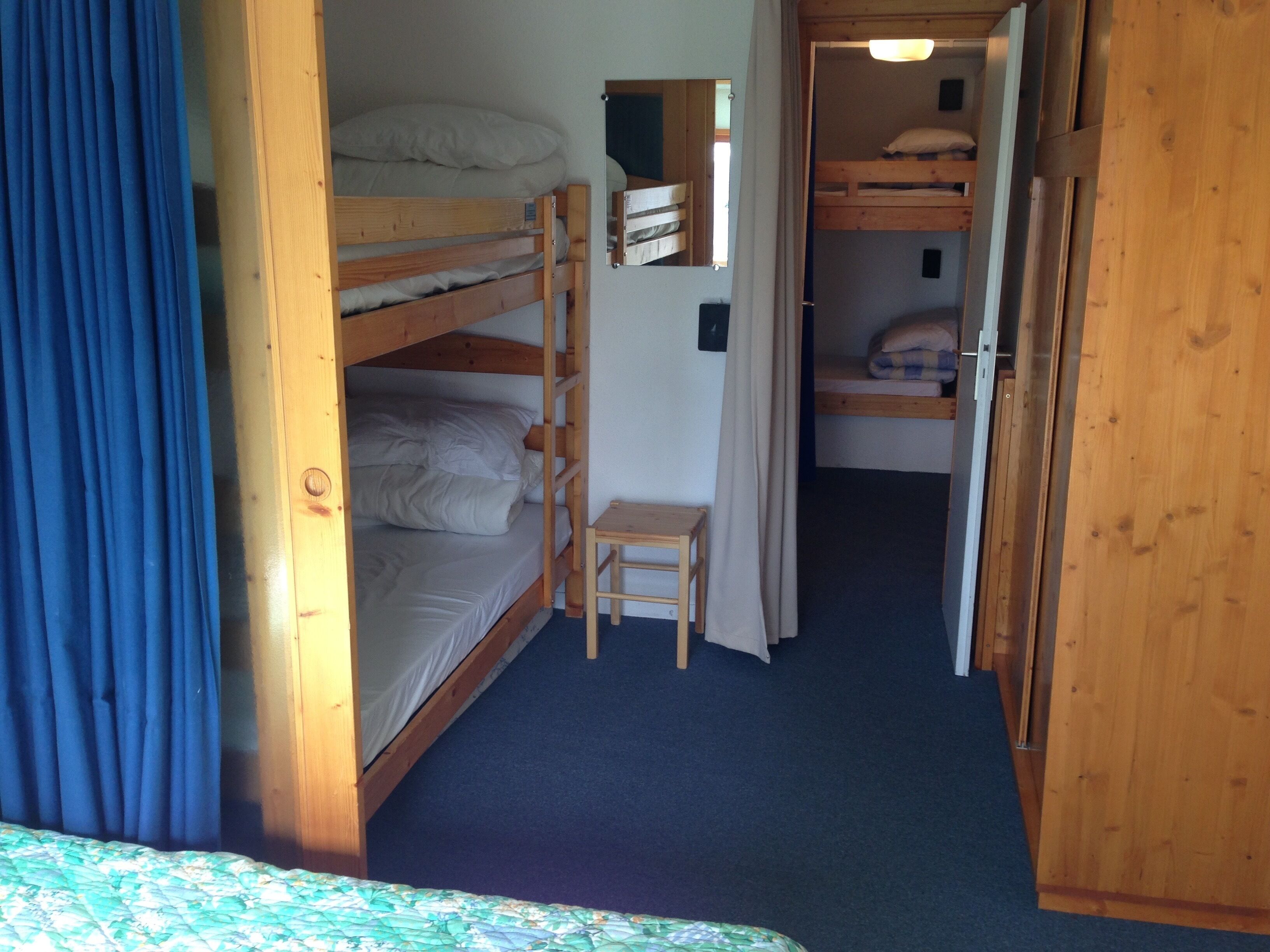 Una habitación con literas, una pequeña mesa de madera y una cortina.