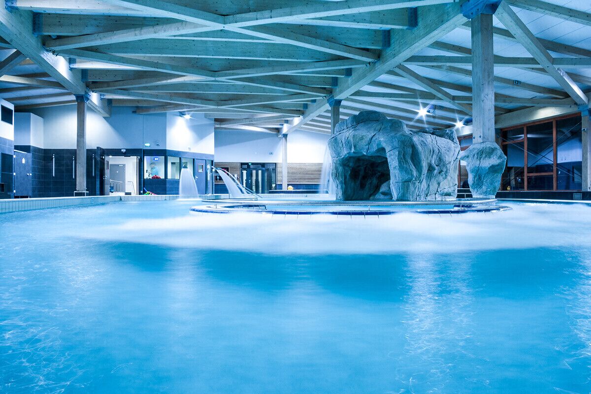 Ein Innenpool mit einem großen Felsen in der Mitte, Holzbalken an der Decke und einer gefliesten Wand.