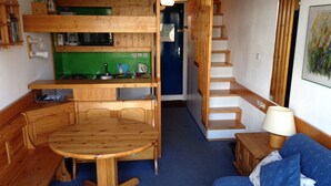 A compact room with a bunk bed, a kitchenette, a dining table, and a sofa.