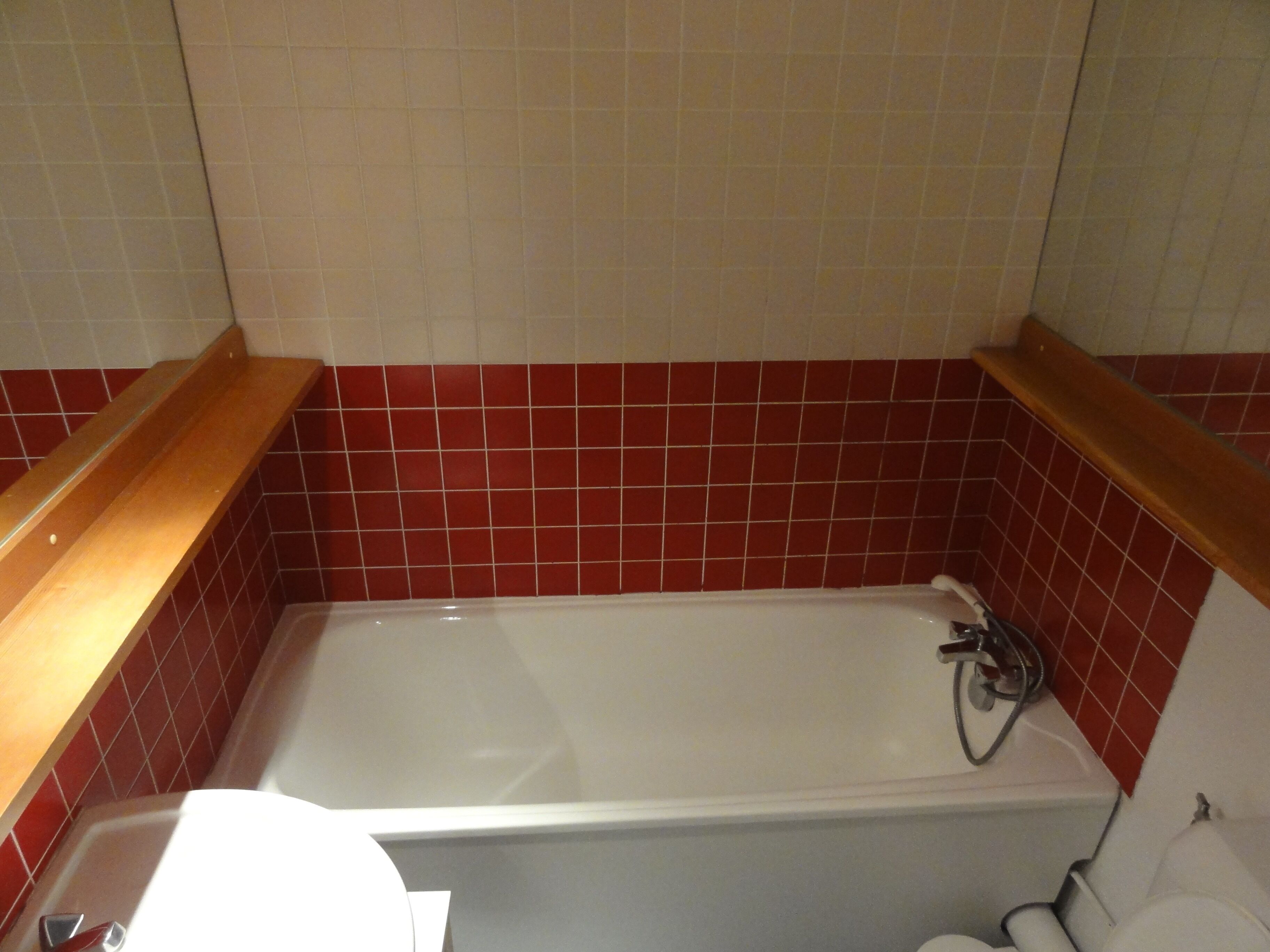 Un baño con bañera, paredes de azulejos rojo y blanco, y estantes de madera.