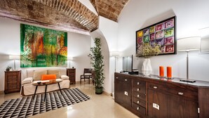 A modern living room with a large abstract painting, a wooden cabinet, and a sofa with an orange cushion. - Casa Becco dos Assucares - free GARAGE - Historic Center (Évora)