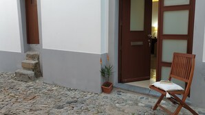 A stone-paved courtyard with a wooden chair and a potted plant. - Casa Becco dos Assucares - free GARAGE - Historic Center (Évora)