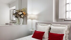 A neatly arranged bedroom with a bed, pillows, a bedside table, a lamp, and a vase of flowers. - Casa Becco dos Assucares - free GARAGE - Historic Center (Évora)