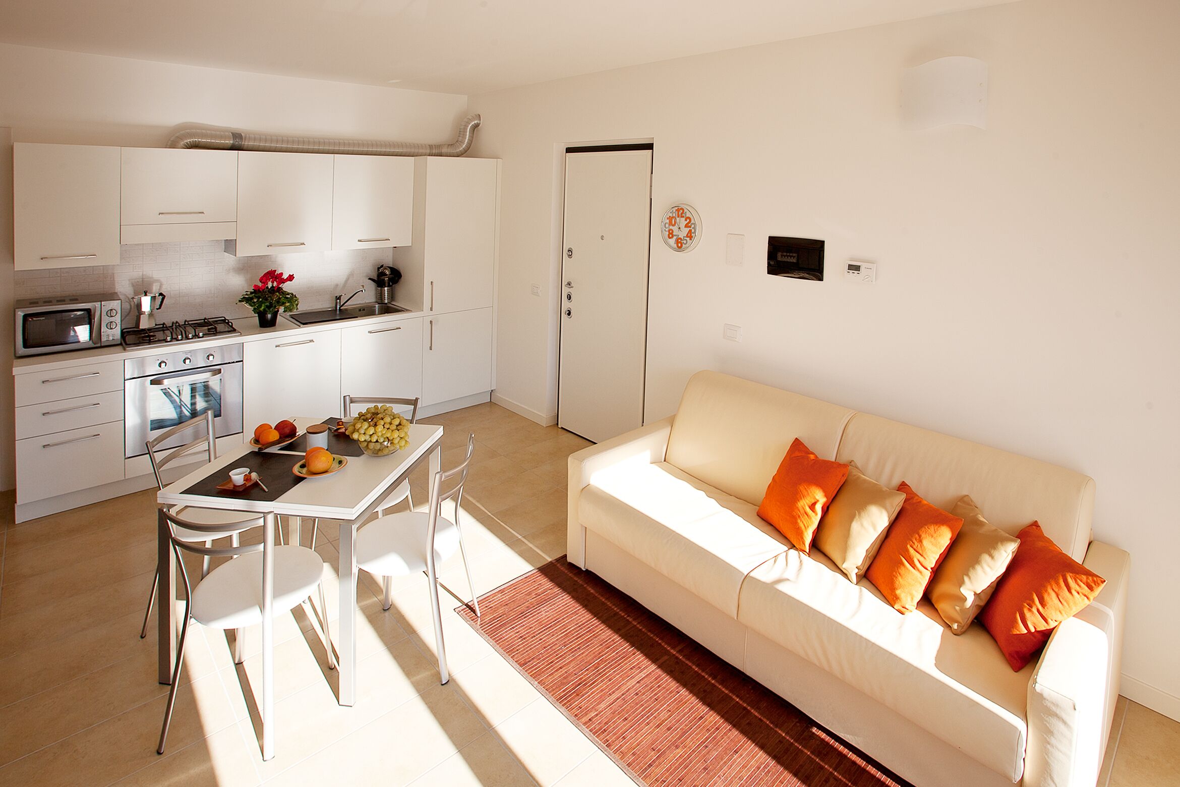 Une cuisine moderne avec des meubles blancs, une table à manger avec des chaises et un canapé blanc agrémenté de coussins orange.