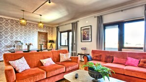 Ein Wohnzimmer mit zwei orangenen Sofas, einem Couchtisch aus Holz mit einer Pflanze und einem Essbereich mit Tisch und Stühlen.
