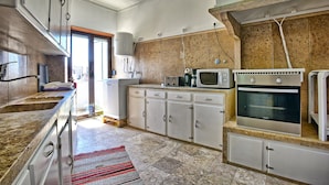 Eine Küche mit Granit-Arbeitsplatten, weißen Schränken, einer Mikrowelle, einem Ofen und einem Fenster mit Blick auf einen Balkon.
