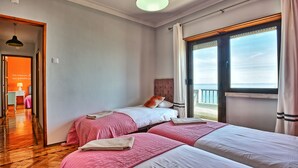 Ein Zimmer mit zwei Betten, Holzboden, einem Vorhangfenster und Meerblick.