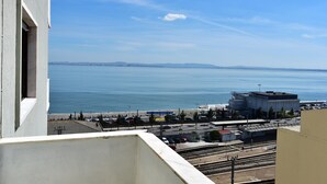 Blick von einem Balkon auf eine Küstenlandschaft mit einem Bahnhof und einem großen Gewässer.