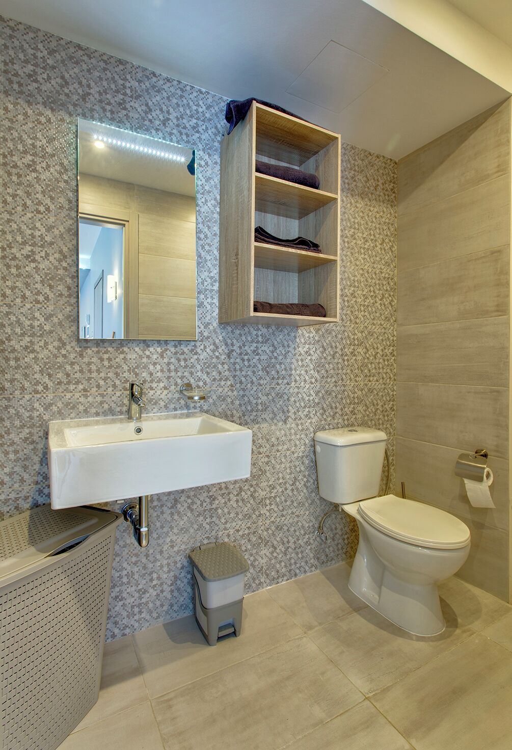 Un baño con un lavabo blanco, un inodoro, un espejo y un estante de madera sobre el lavabo.