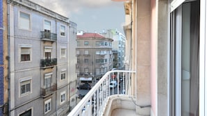 Un balcone con vista su edifici vicini, una strada sottostante e un cielo sereno.