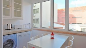 Una piccola cucina accessoriata con lavatrice, bollitore ed un tostapane. Si nota un tavolo con una lanterna rossa e sedie bianche.