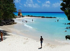 Una playa con agua turquesa cristalina, una torre de salvavidas y gente nadando y caminando sobre la arena.