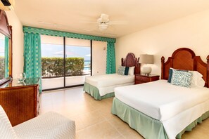 A hotel room with two beds, a ceiling fan, a nightstand with a lamp, and a view of the sea through large windows. - Stunning Calypso - Beachfront & Poolside ! (Christ Church)