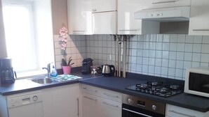 Una cucina compatta con mobili bianchi, un fornello a gas, un forno a microonde e un lavello.