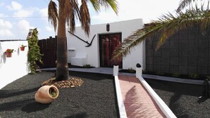 A modern outdoor area with a palm tree, a white building with a red door, and a pathway leading to the entrance.