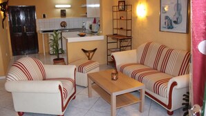 A living room with striped sofas, a wooden coffee table, and a kitchen in the background.