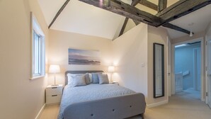 A bedroom with a large bed, two bedside tables, a ceiling with exposed beams, a painting on the wall, and a door leading to another room. - Central Windsor Apartment Facing The Castle (Windsor)