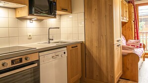 Een compacte keuken met houten kastjes, een magnetron, een oven en een vaatwasser.