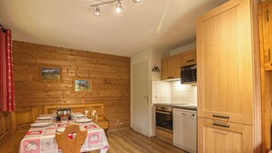 Een houten interieur met een eettafel voor vier personen, een keuken met witte kasten en apparatuur, en een houten vloer.