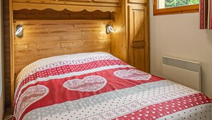 Een slaapkamer met een houten hoofdbord, een bed met een rood-wit gebedrukte spreidekker en een raam met uitzicht op bomen.