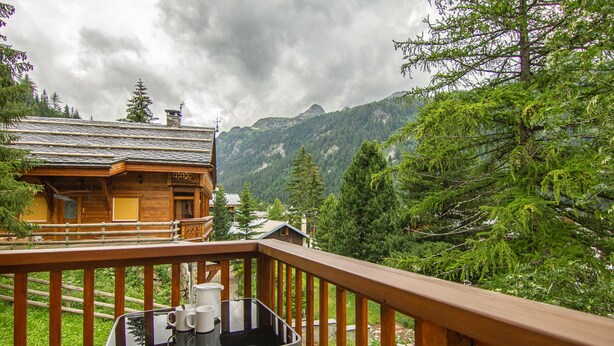 Een houten hut met een balkon dat uitkijkt over een bergachtig landschap.