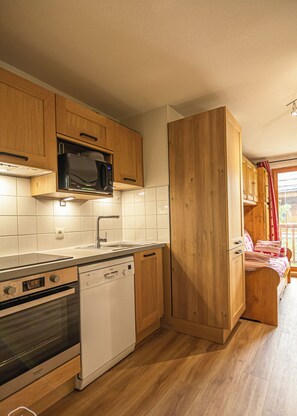 A compact kitchen with wooden cabinets, a microwave, an oven, and a dishwasher.
