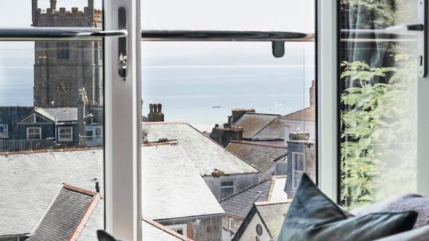 A room with a large window offering a view of a historic building and a clear sky. - Heart of St Ives, Parking, Superb Views, Sleeps 6 (Saint Ives)