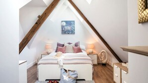 A bedroom with a sloped ceiling, a bed with striped bedding, two bedside tables with lamps, a decorative wall piece, and a wooden bench. - Heart of St Ives, Parking, Superb Views, Sleeps 6 (Saint Ives)