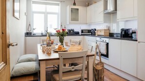 A modern kitchen with white cabinets, a wooden dining table, and a window providing natural light. - Heart of St Ives, Parking, Superb Views, Sleeps 6 (Saint Ives)