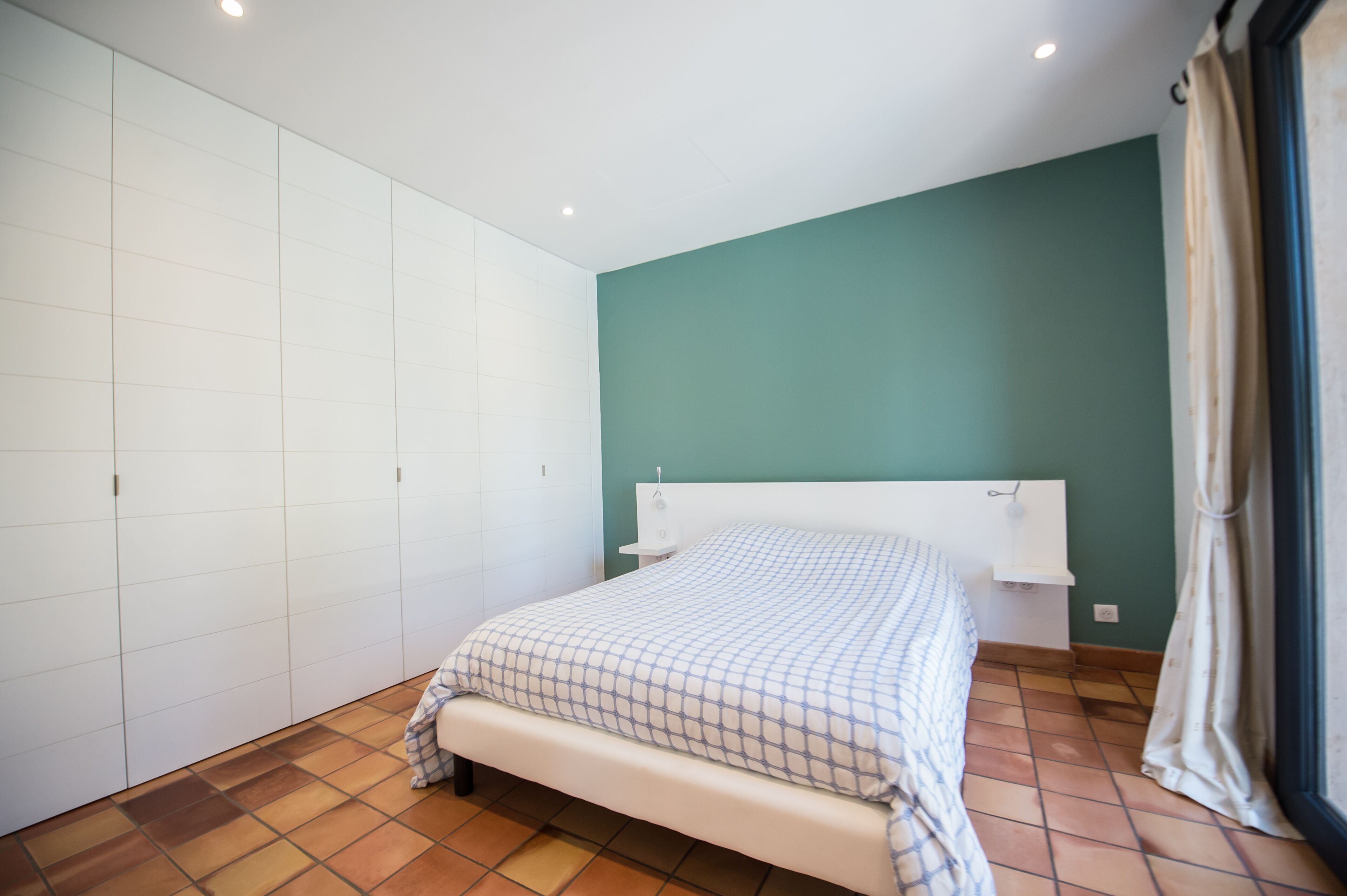 Un dormitorio con cama, armario y ventana con cortinas.