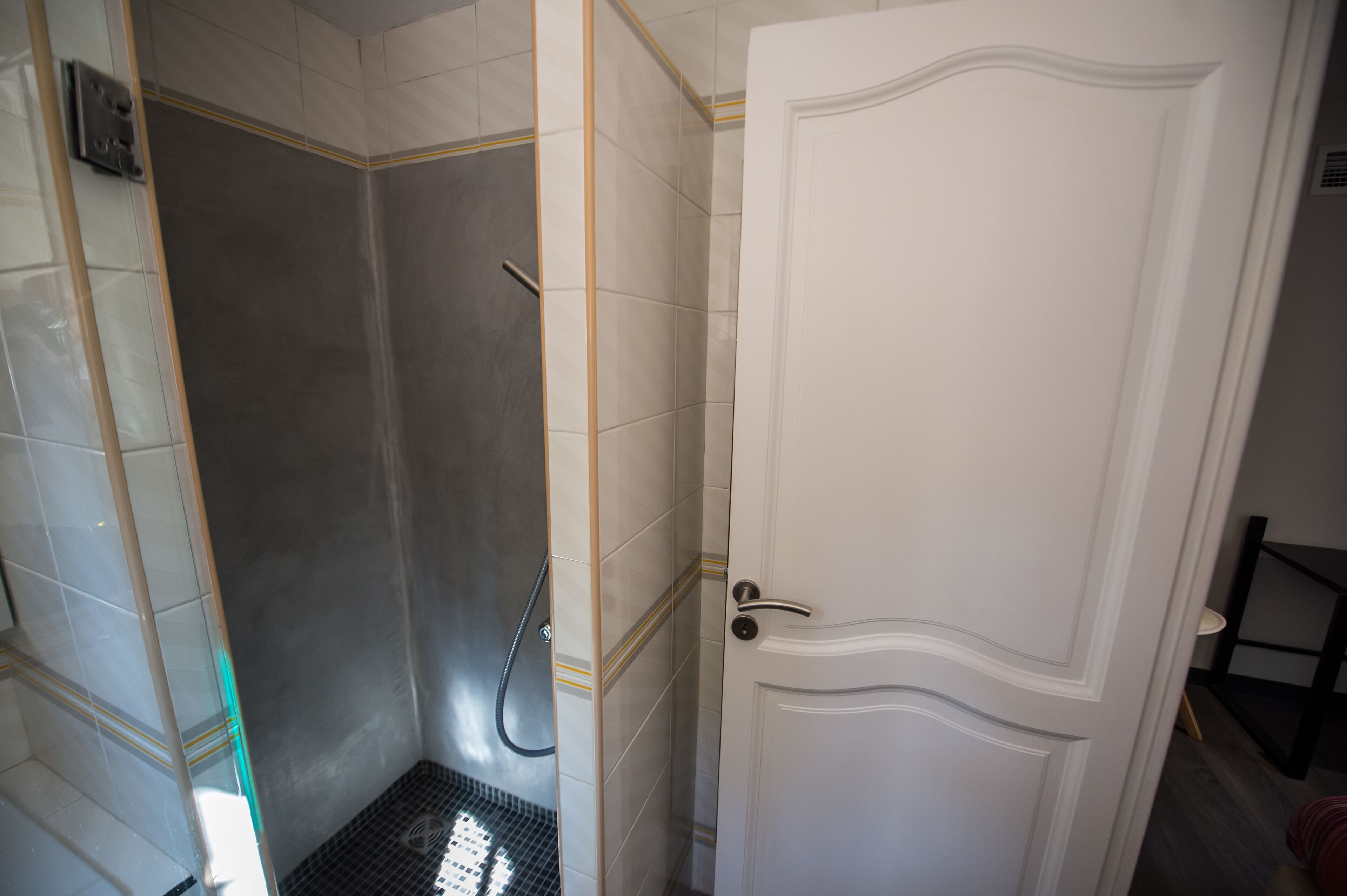 A bathroom with a shower, a white door, and tiled walls.