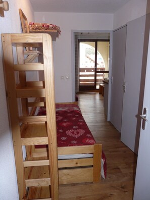 Cozy single room with a wooden bunk bed and a small chair, featuring a window with an outside view.