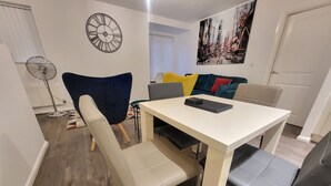 Ein Essbereich mit einem weißen Tisch, beigen Stühlen, einem blauen Sofa und einer Uhr an der Wand.