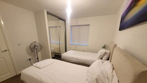 Ein Zimmer mit zwei Betten, einem Ventilator, einem Fenster mit Jalousien und einer Tür.