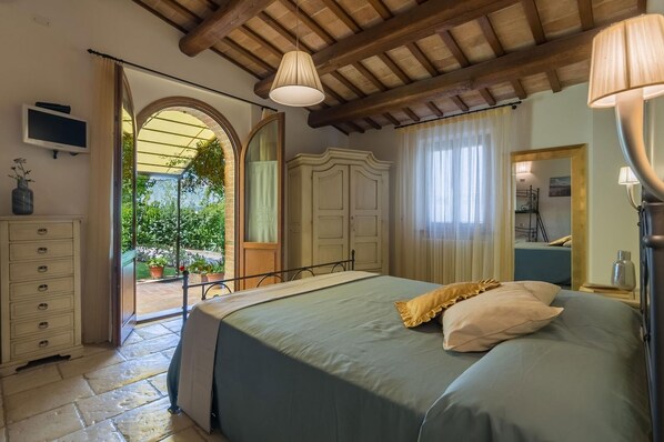 A bedroom with a bed, a dresser, a wardrobe, and a mirror. There is a window with curtains and a view of greenery outside. - Villa Design - Private villa, 3 bedrooms, pool, A/C, wifi, EV charger, Marche (Pergola)